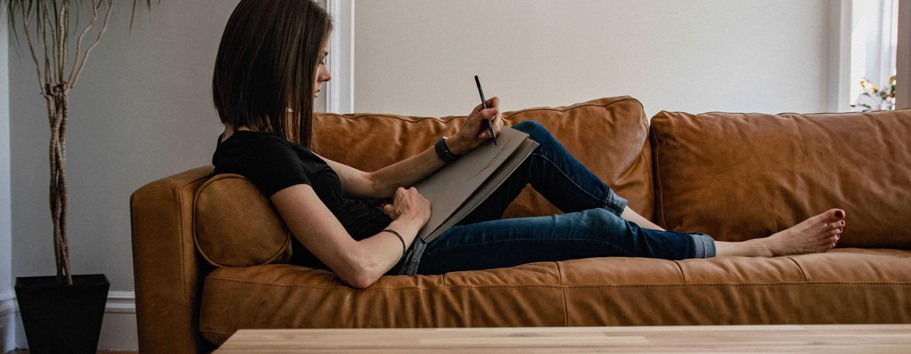 woman lies on a couch and draws on a large sketch pad